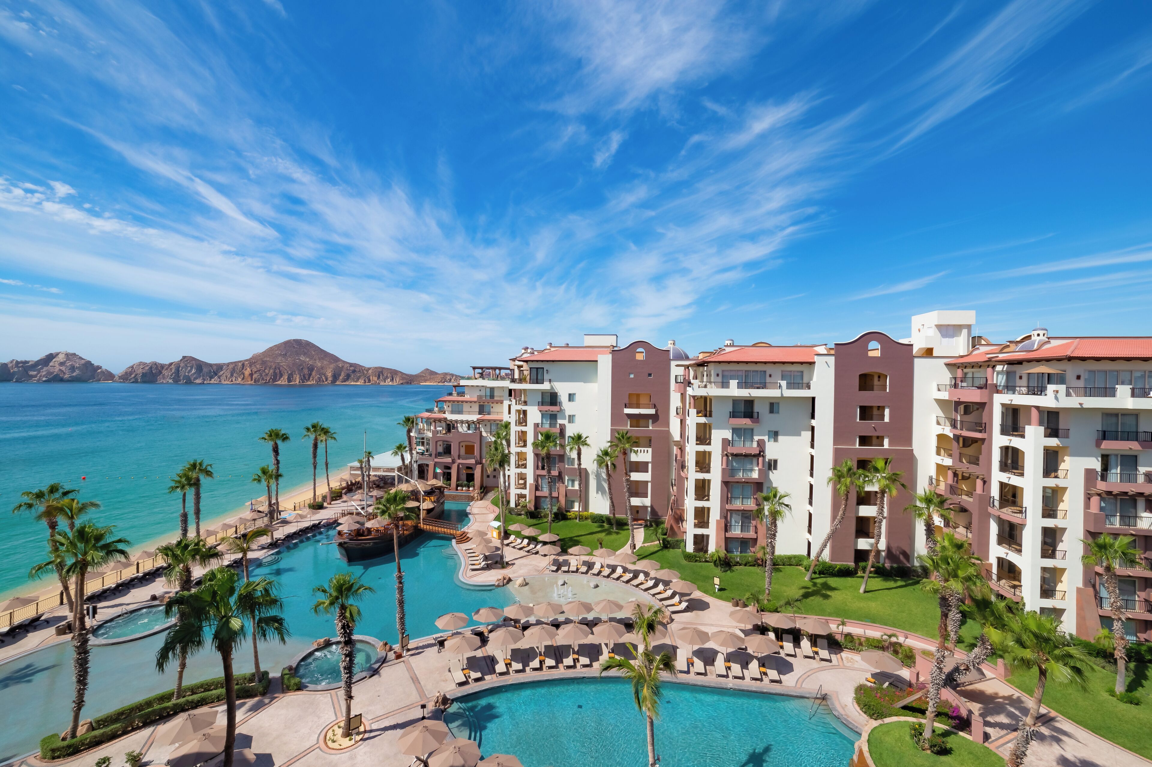 A resort with multiple buildings, a swimming pool, and palm trees.