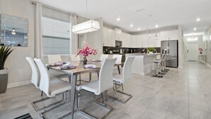 A modern kitchen with white cabinets, stainless steel appliances, and a dining area with white chairs and a glass table.