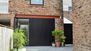 A brick building with a large black garage door, a small window, and potted plants in the foreground.