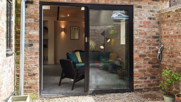 A brick building with a sliding glass door leading to a living area with a sofa and a coffee table.