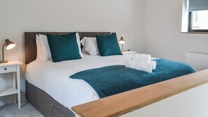 A neatly made bed with white and teal bedding, two bedside lamps, and a wooden bench at the foot of the bed.
