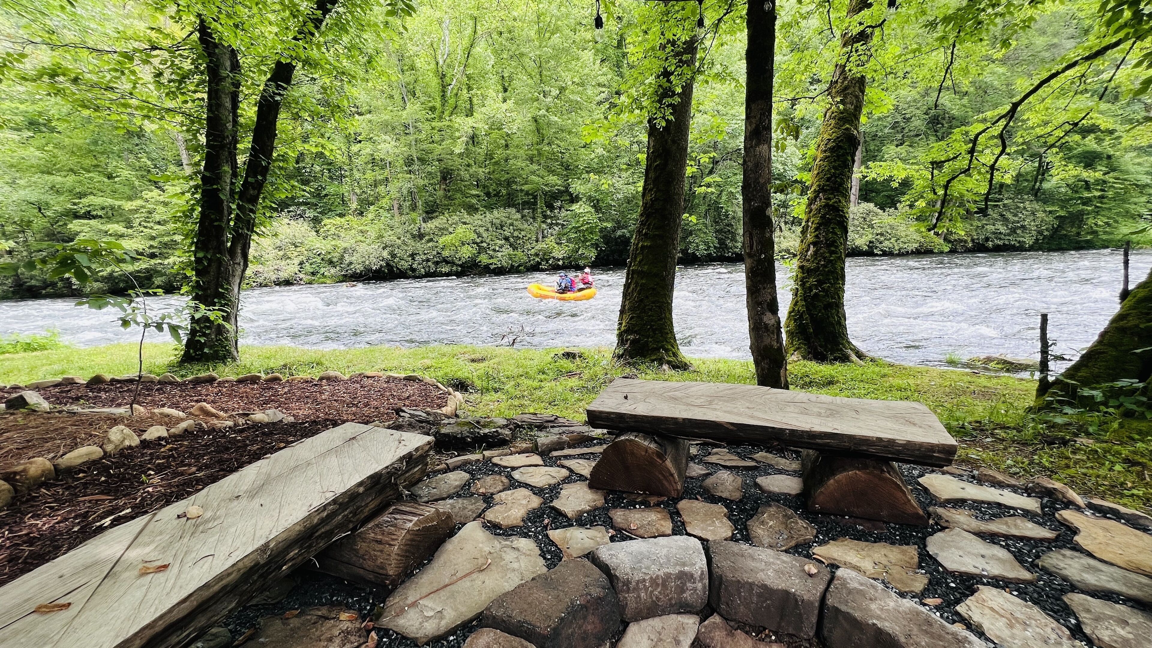 Un espace de pique-nique au bord de la rivière, équipé d’un banc en bois et d’un foyer.