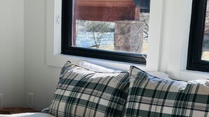 Een bed met geruit beddengoed en een raam met uitzicht op een gebouw.