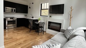 Een moderne keuken met een eethoek, een grijze bank met gekleurde kussens en een houten plafond.