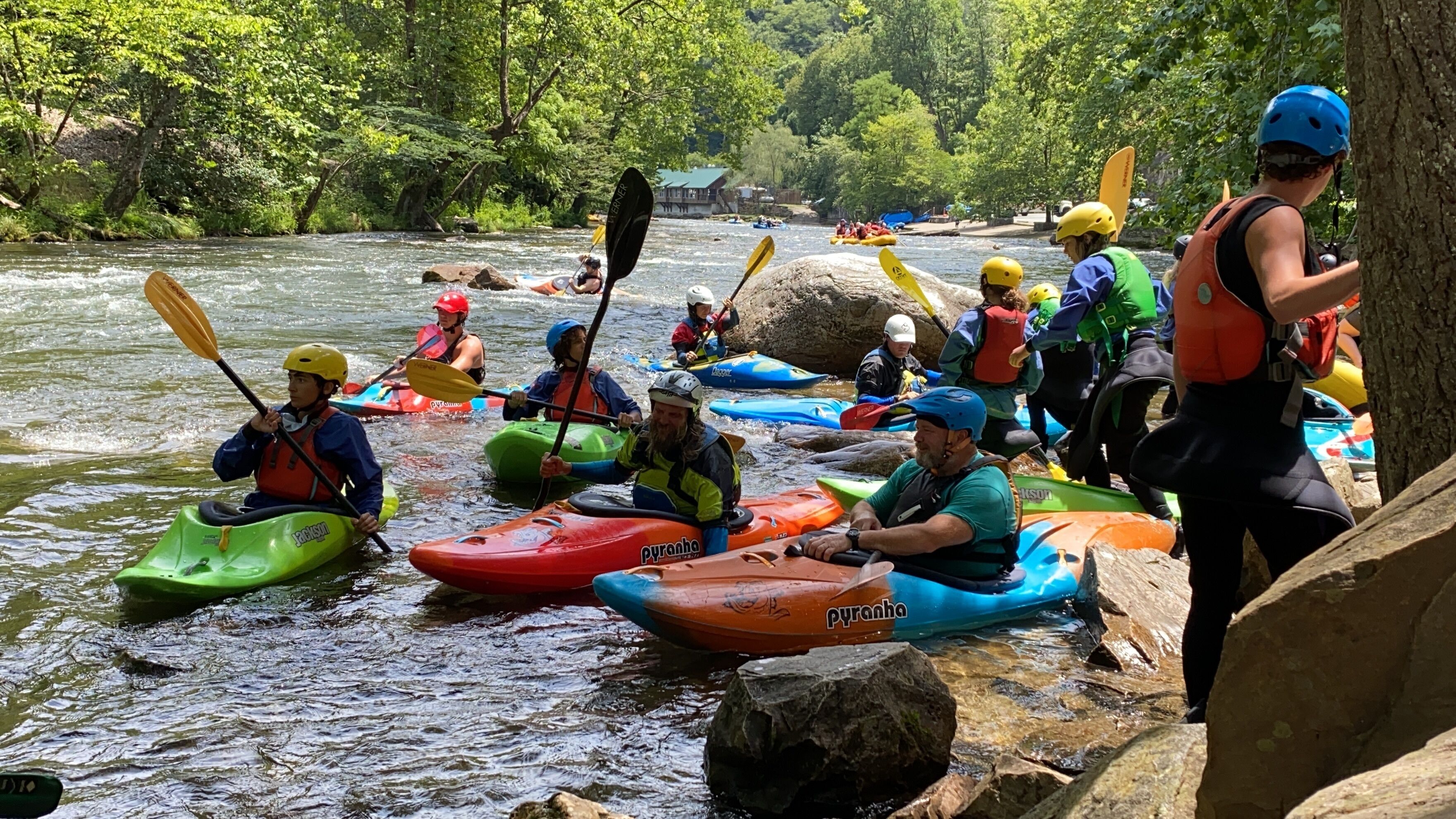 A group of people kayaking on a river surrounded by trees.