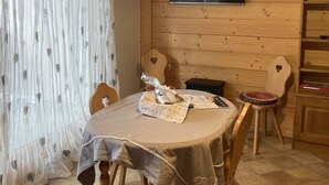 Un rincón comedor acogedor con una mesa de madera, sillas, un televisor montado en la pared y una estantería.