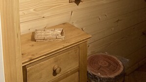 Interior de una cabaña de madera con una ventana, un aparador de madera y recortes en forma de corazón en la pared.