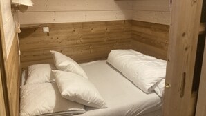 Una habitación de madera pequeña y acogedora con una cama individual, ropa de cama blanca, una lámpara de pared y un armario de madera con diseños de corazones.