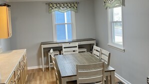 A dining area with a wooden table and chairs, a window with a patterned valance, and a light fixture above.