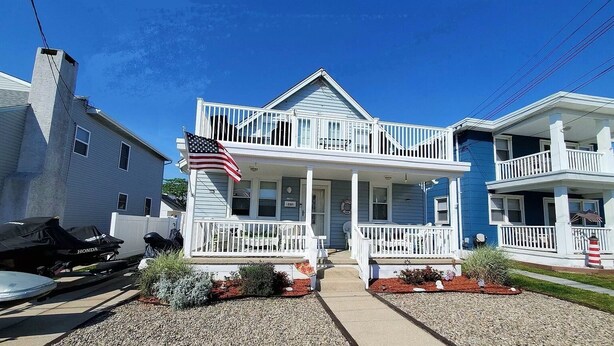 A two-story house with a porch, a flag, and a small garden.