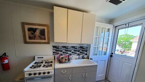 A compact kitchen with a gas stove, a white oven, grey cabinets, and a tiled backsplash.