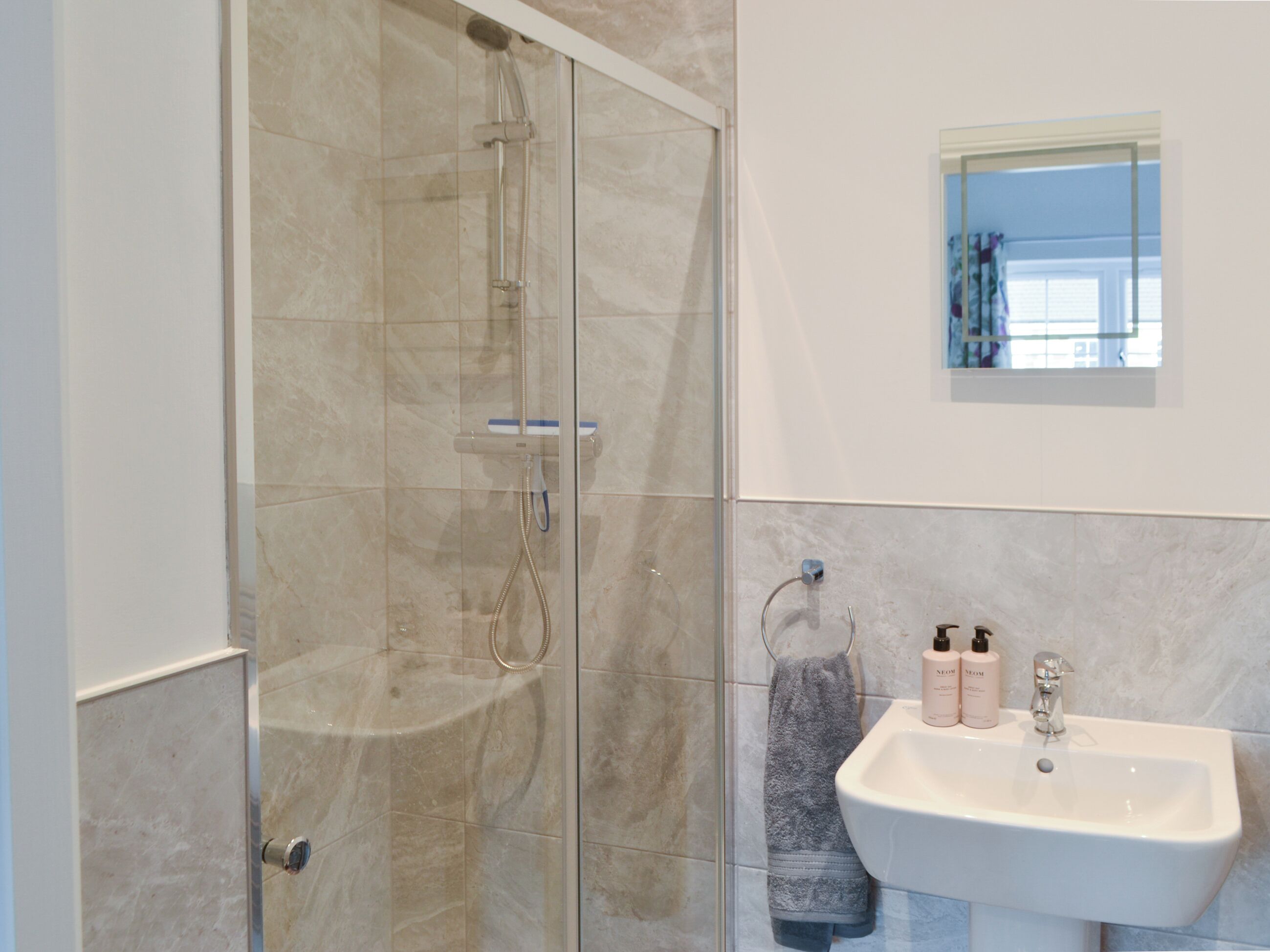 Een badkamer met een douchecabine, een wastafel met toiletartikelen en een raam met uitzicht.
