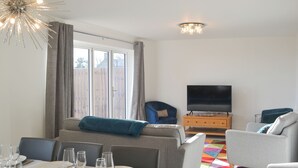 A modern living room with a sofa, a television, and a dining area set with plates and glasses. - 4 bedroom accommodation in Acklington, near Warkworth (Acklington, near Warkworth)