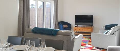 A modern living room with a sofa, a television, and a dining area set with plates and glasses.