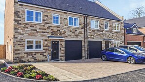 A two-story house with a stone facade, two garage doors, and a blue car parked in the driveway. - 4 bedroom accommodation in Acklington, near Warkworth (Acklington, near Warkworth)