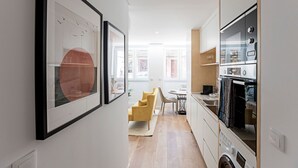 Een moderne keuken met een inbouwoven, een wasmachine, en een eethoek met een gele stoel en tafel.