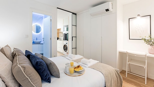 Een moderne hotelkamer met een bed, een ontbijttafel, een wasmachine en een spiegel.