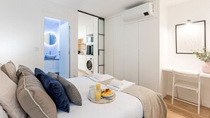 Una habitación de hotel moderna con cama, bandeja de desayuno, lavadora y espejo.