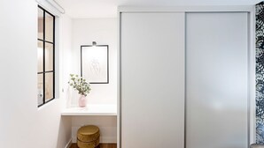 Un couloir avec une porte coulissante, une œuvre d’art encadrée au mur, une petite fenêtre avec une plante et un tabouret rond.