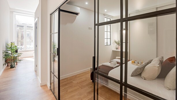 Une chambre d’hôtel moderne avec une cloison en verre, un lit avec des oreillers, une table de chevet sur laquelle se trouve un plateau de petit-déjeuner et une plante en pot.