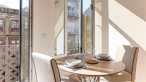 Un coin repas avec une table ronde, deux chaises et une vue sur les bâtiments à travers de grandes fenêtres.