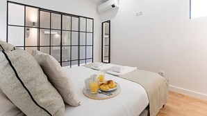 Una habitación de hotel moderna con una cama grande, una bandeja de desayuno con cruasanes y jugo de naranja, y vistas a través de un ventanal.