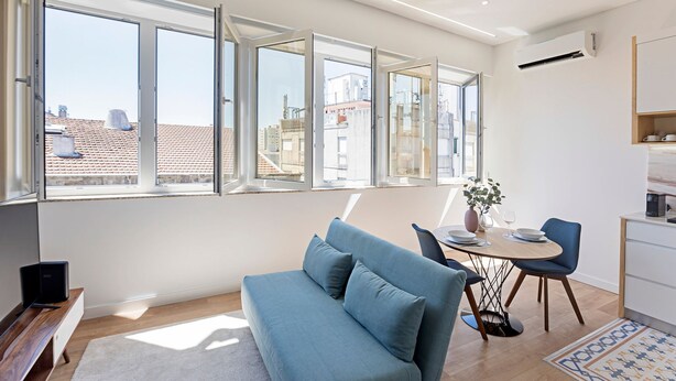 Una sala de estar moderna con sofá, mesa de comedor, sillas y vistas de la ciudad a través de amplias ventanas.