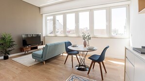 Una sala moderna con sofá, dos sillones, una mesa de comedor, televisor y un ventanal con vistas a la ciudad.