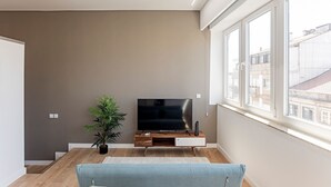 Una sala de estar con un televisor de pantalla plana sobre un soporte de madera, una planta en maceta y un sofá azul.