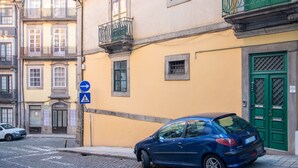 Ein blaues Auto parkt auf einer Kopfsteinpflasterstraße neben einem gelben Gebäude mit grüner Tür und einem Balkon.