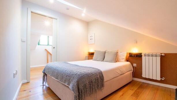 Ein Schlafzimmer mit Bett, Nachttischlampen, Heizkörper und einer Tür, die auf einen Balkon führt.
