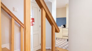 A wooden staircase leading to a room with a white door, a kitchen with blue tiles, and a patterned floor.