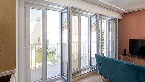 A modern living room with a teal sofa, a flat-screen TV, and a sliding glass door leading to a balcony. - Urban House - D - by LovelyStay (Porto)