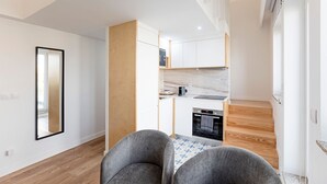 Moderni keittiö, jossa on sisäänrakennettu uuni ja mikroaaltouuni, ruokailutila, jossa on kaksi harmaata tuolia, sekä suuri peili seinällä.