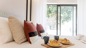 A bed with pillows, a tray with croissants and a mug, and a view of greenery through a window. - Paraíso -1B w/ AC & Patio by LovelyStay (Porto)