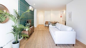 A modern living room with a white sofa, a wooden coffee table, and a large potted plant. - Paraíso -1B w/ AC & Patio by LovelyStay (Porto)