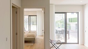 A modern bedroom with a bed, a small seating area with a chair, and a balcony with a table and chairs. - Paraíso -1B w/ AC & Patio by LovelyStay (Porto)