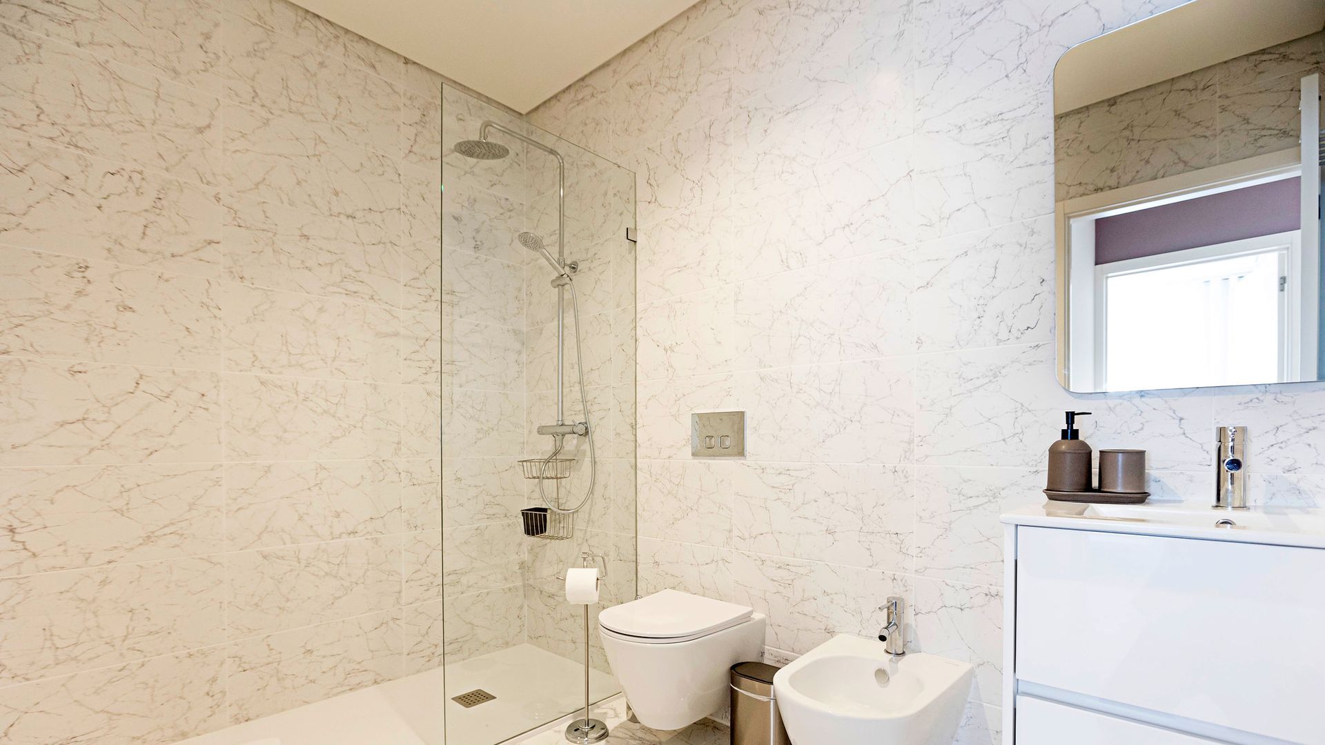 A modern bathroom with a glass-enclosed shower, a toilet, a bidet, and a sink with a mirror above.
