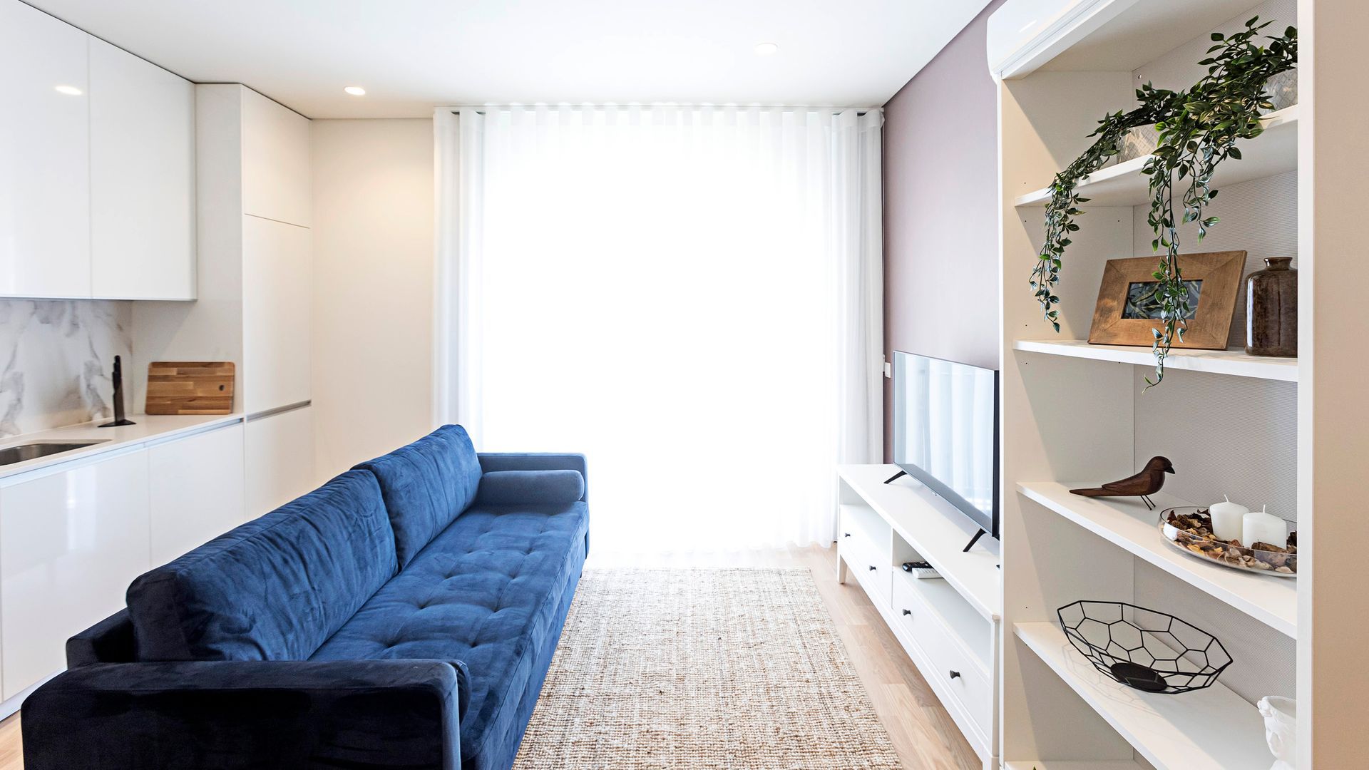Ein modernes Wohnzimmer mit einem blauen Sofa, einem Flachbildfernseher und einem weißen Konsolentisch mit Dekoration.