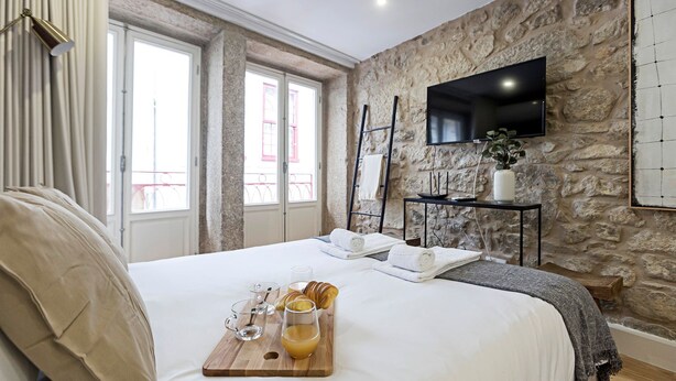Habitación de hotel con pared de piedra, cama con ropa blanca, bandeja con alimentos para el desayuno y televisor de pantalla plana montado en la pared.