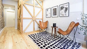 Una habitación con piso de madera, un tapete blanco y negro a lunares, dos sillones de cuero, una pequeña mesa de madera con un altavoz y tres cuadros en la pared.