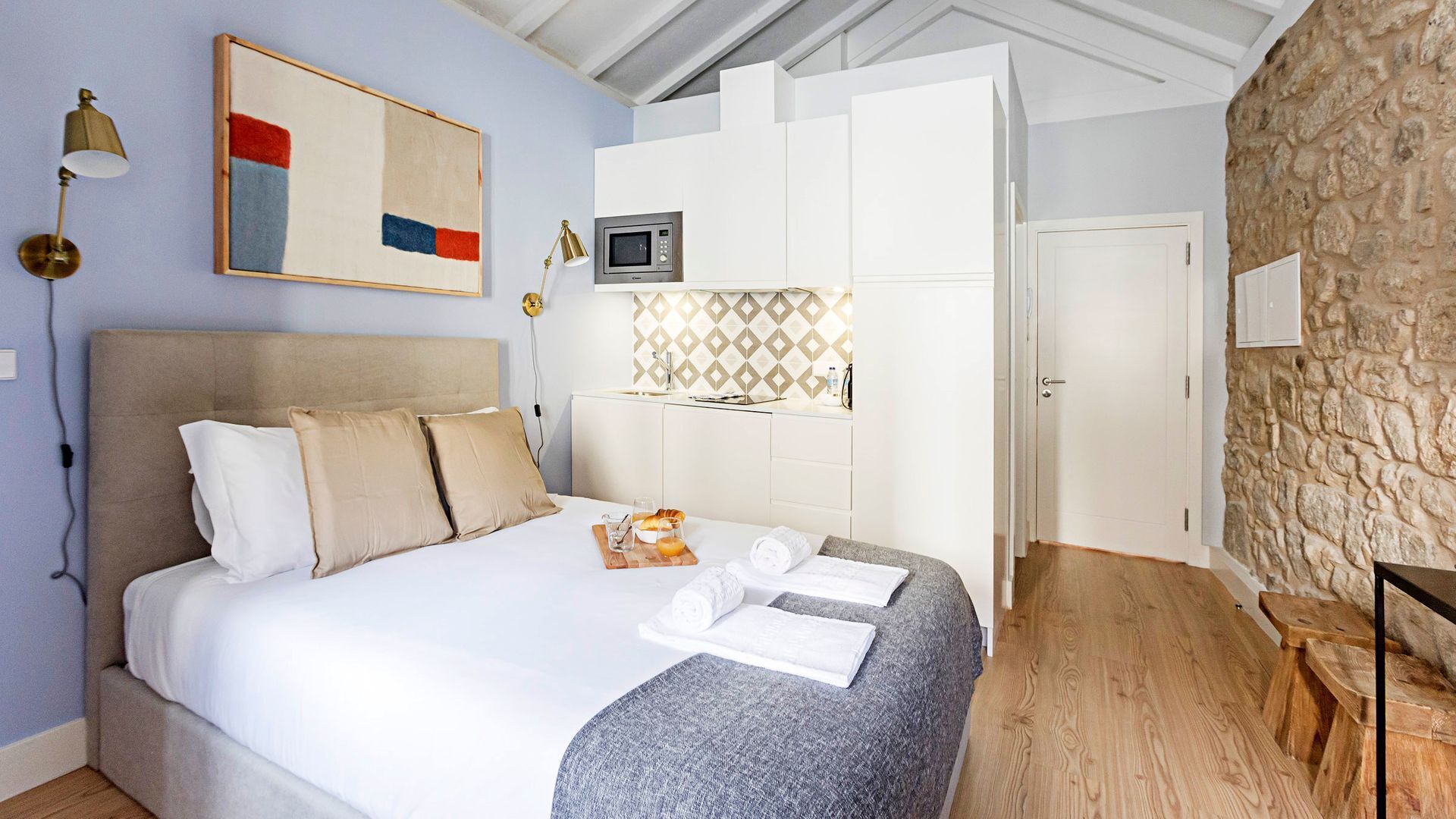 Ein Schlafzimmer mit Bett, Nachttisch, Lampe, Gemälde, Mikrowelle und einer Steinwand.
