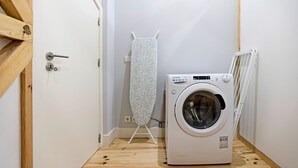 Uma lavanderia compacta com máquina de lavar, tábua de passar e radiador.