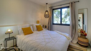 A bedroom with a large bed, a bedside lamp, a window with curtains, and a mirror. - Bergerie, Panoramic sea view, Heated pool, Gr20 access (Sari-Solenzara)
