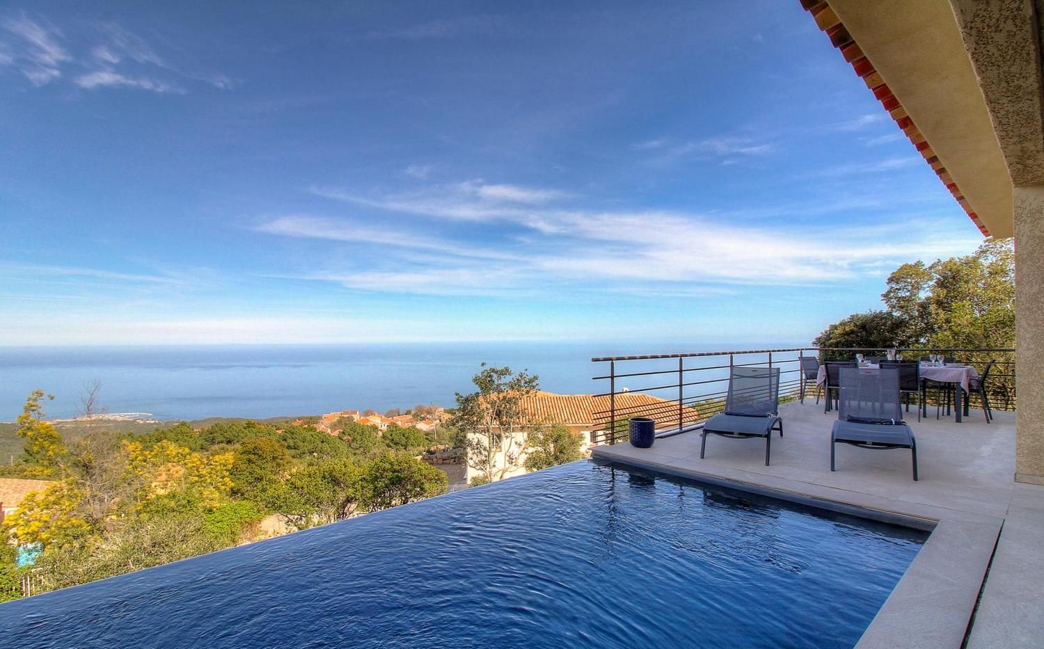 A swimming pool with a view of the sea and a patio area with chairs and tables.