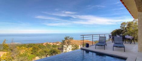 A swimming pool with a view of the sea and a patio area with chairs and tables.