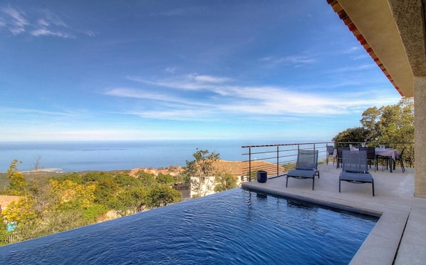 A swimming pool with a view of the sea and a patio area with chairs and tables.