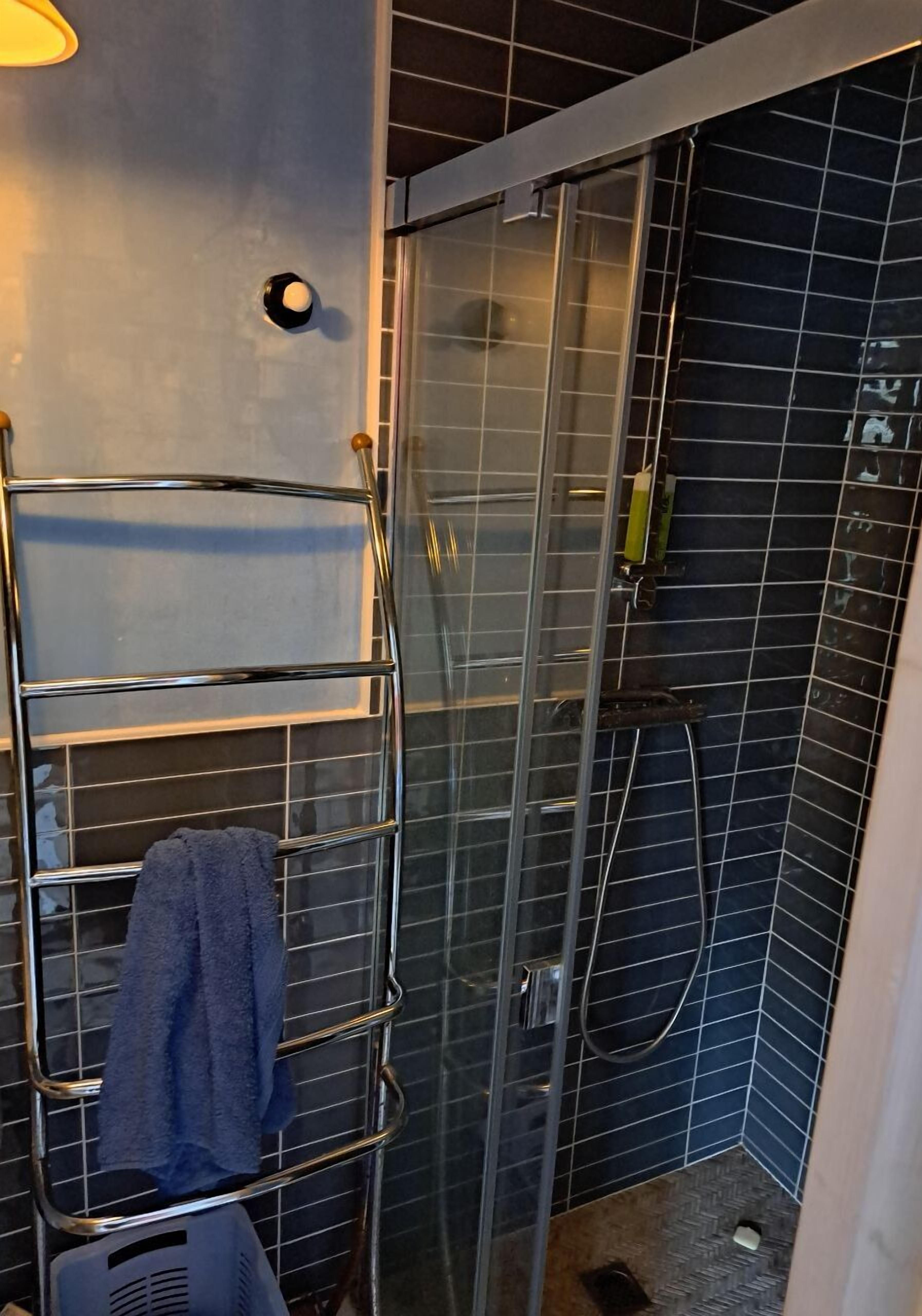 Un baño con cabina de ducha de vidrio, un perchero con toalla y un cabezal de ducha.