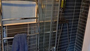 Une salle de bain avec une douche à parois de verre, un porte-serviettes avec une serviette et un pommeau de douche.