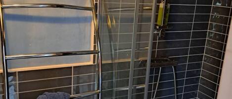 Un baño con cabina de ducha de vidrio, un perchero con toalla y un cabezal de ducha.